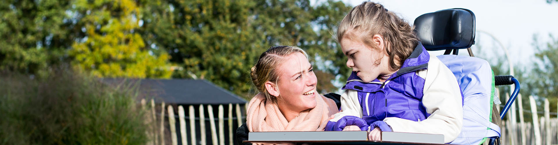 Young girl with disabilities riding in an assisted mobility device with a caregiver by her side