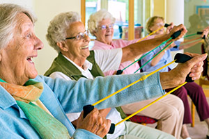 elderly women in an exercise class sitting on chairs and stretching bands with hands