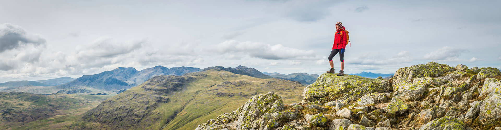Teenage girl hiker standing on a mountain summit overlooking a panoramic vista of green valleys and rocky peaks high in the picturesque natural landscape of the Lake District National Park, Cumbria, UK. ProPhoto RGB profile for maximum color fidelity and gamut.