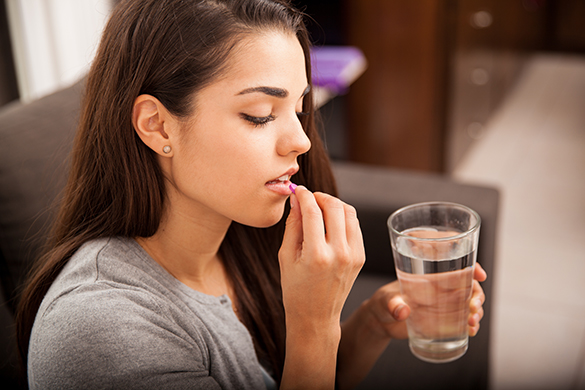 Cute young brunette taking a pill with a glass of water at home
