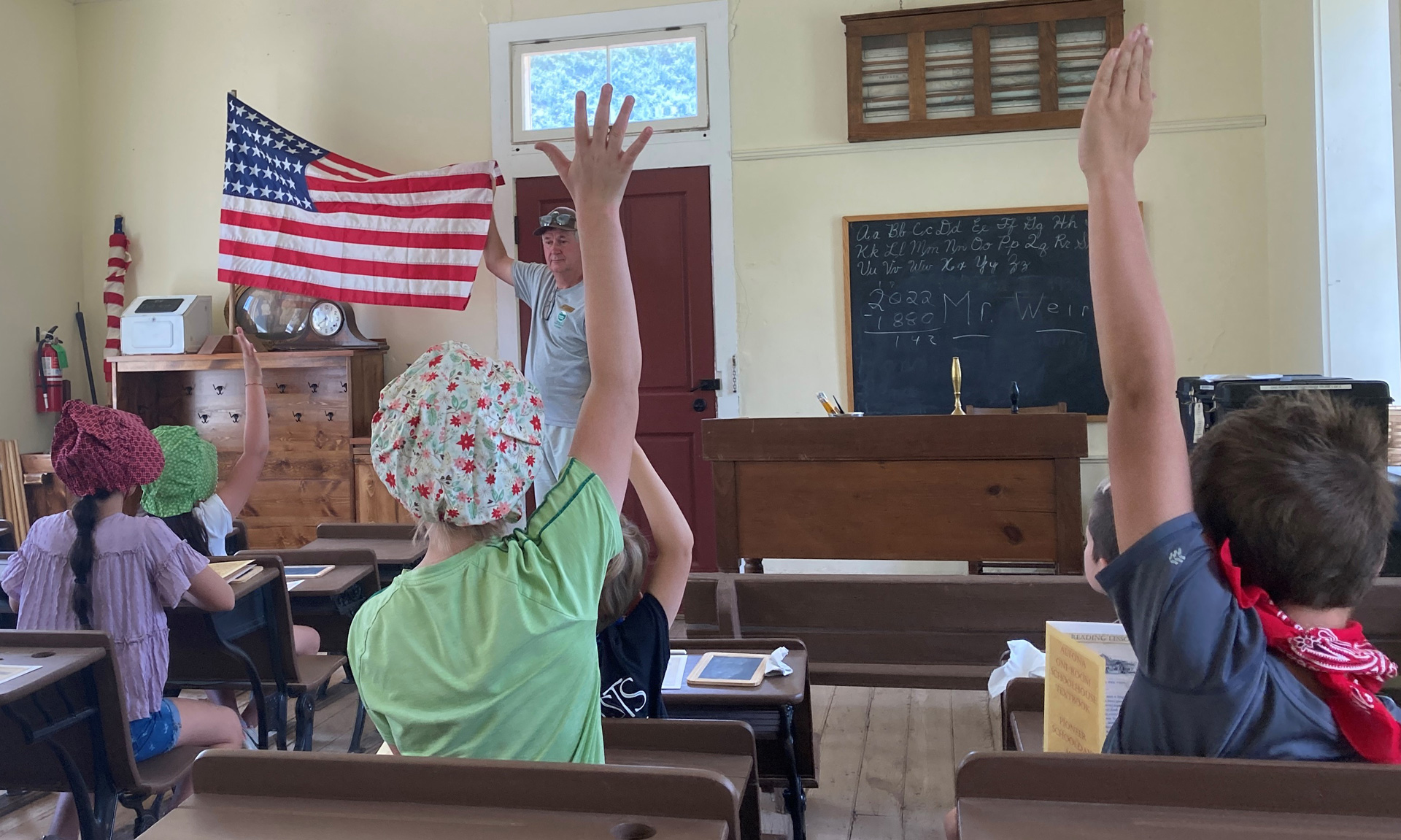 A group of children raise their hands inside the historic Altona Schoolhouse