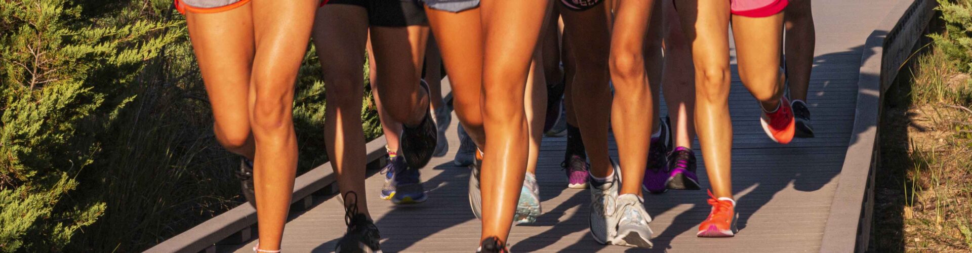 Legs of female runners in shorts running in the sunshine on a boardwalk at the beach