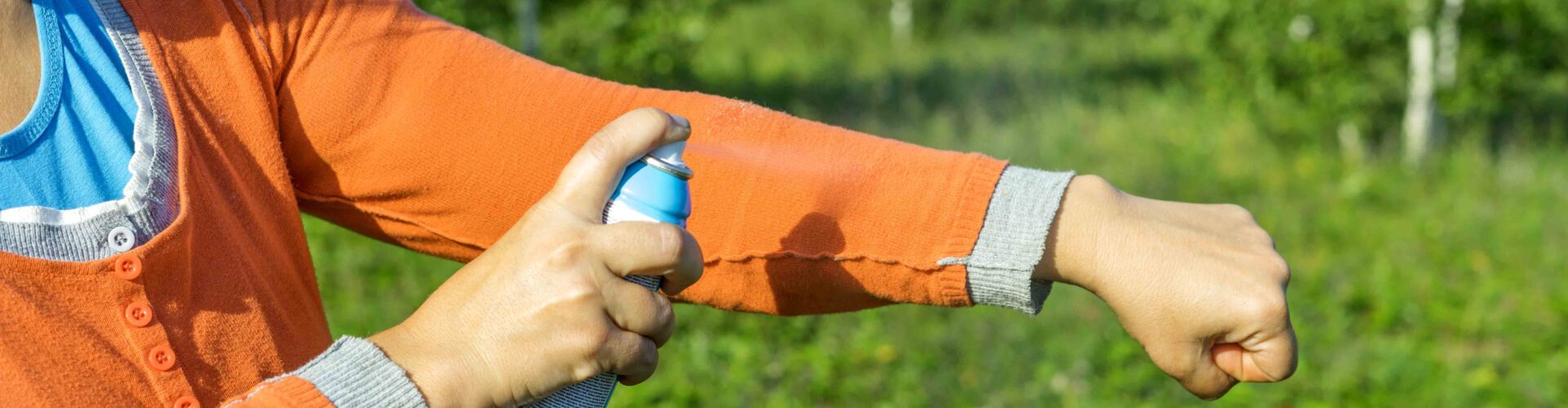 person applying insect repellent on long sleeves