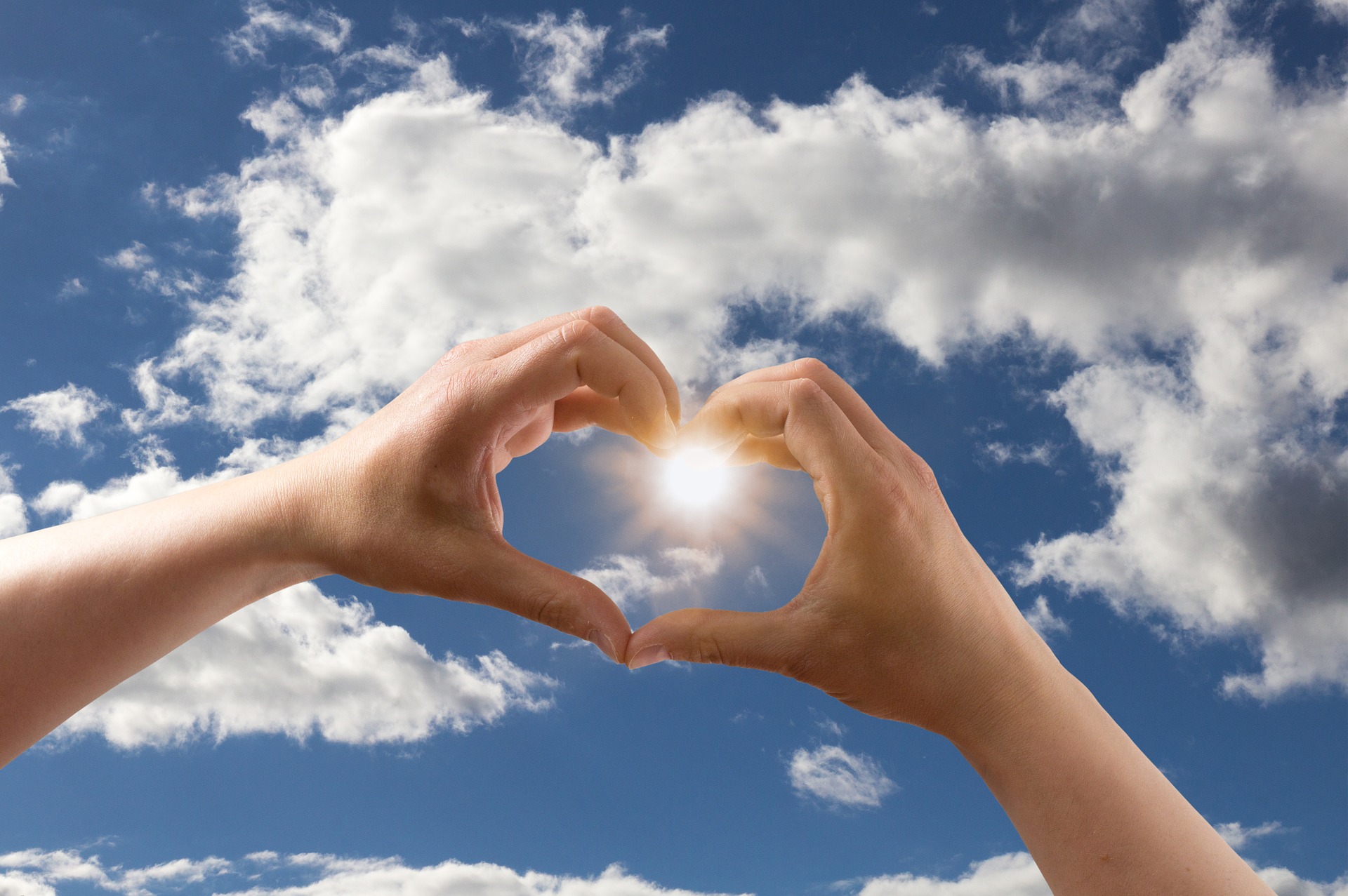 two hands making a heart shape with sky and clouds behind them