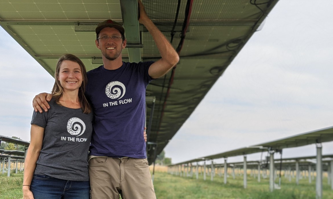 A man and a woman smiling underneath a solar panel
