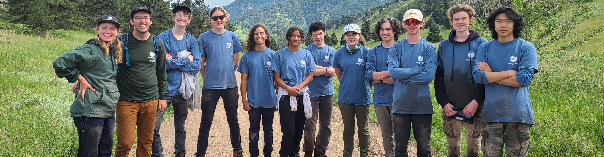 12 Youth Corps workers stand in a line on a trail with mountains in the background