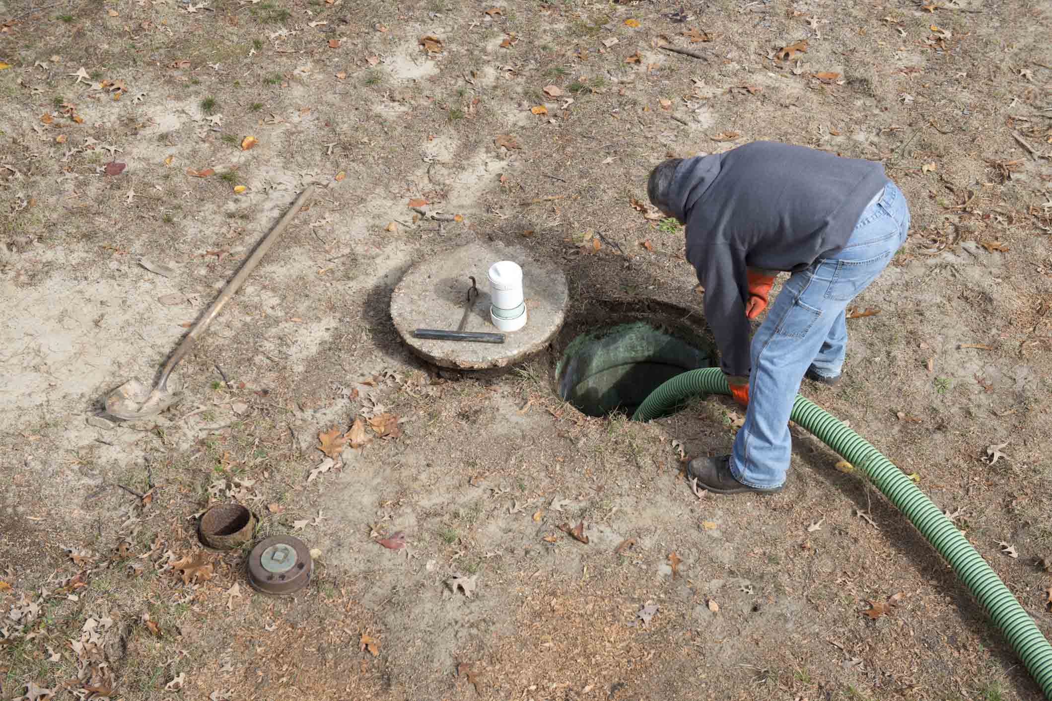 Septic worker inserts hose to pump home sewage from septic tank.