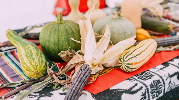 Local native produce including gourds and corn sit on a table with multicolored tablecloth
