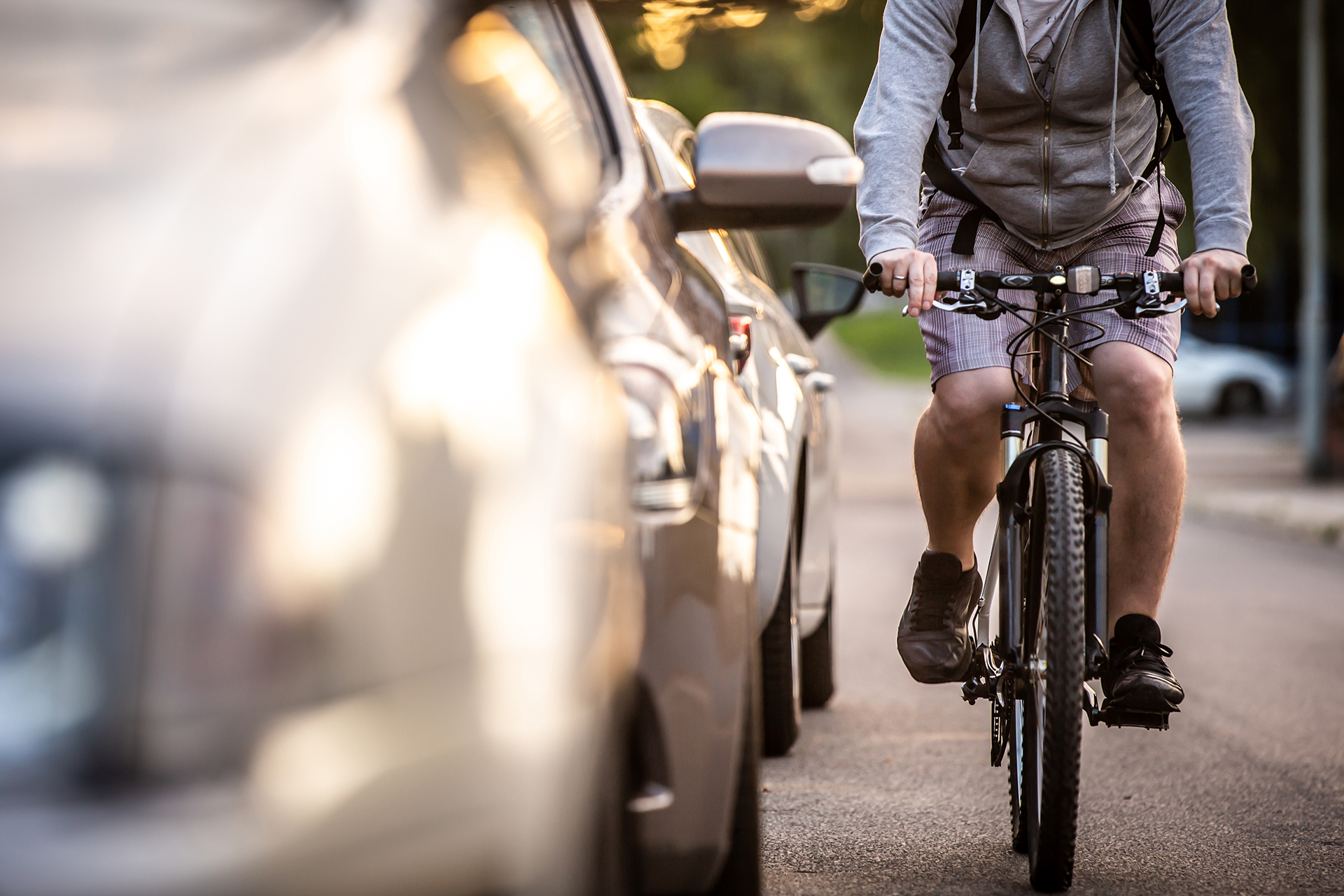 A cyclist riding beside a row of parked cars.
