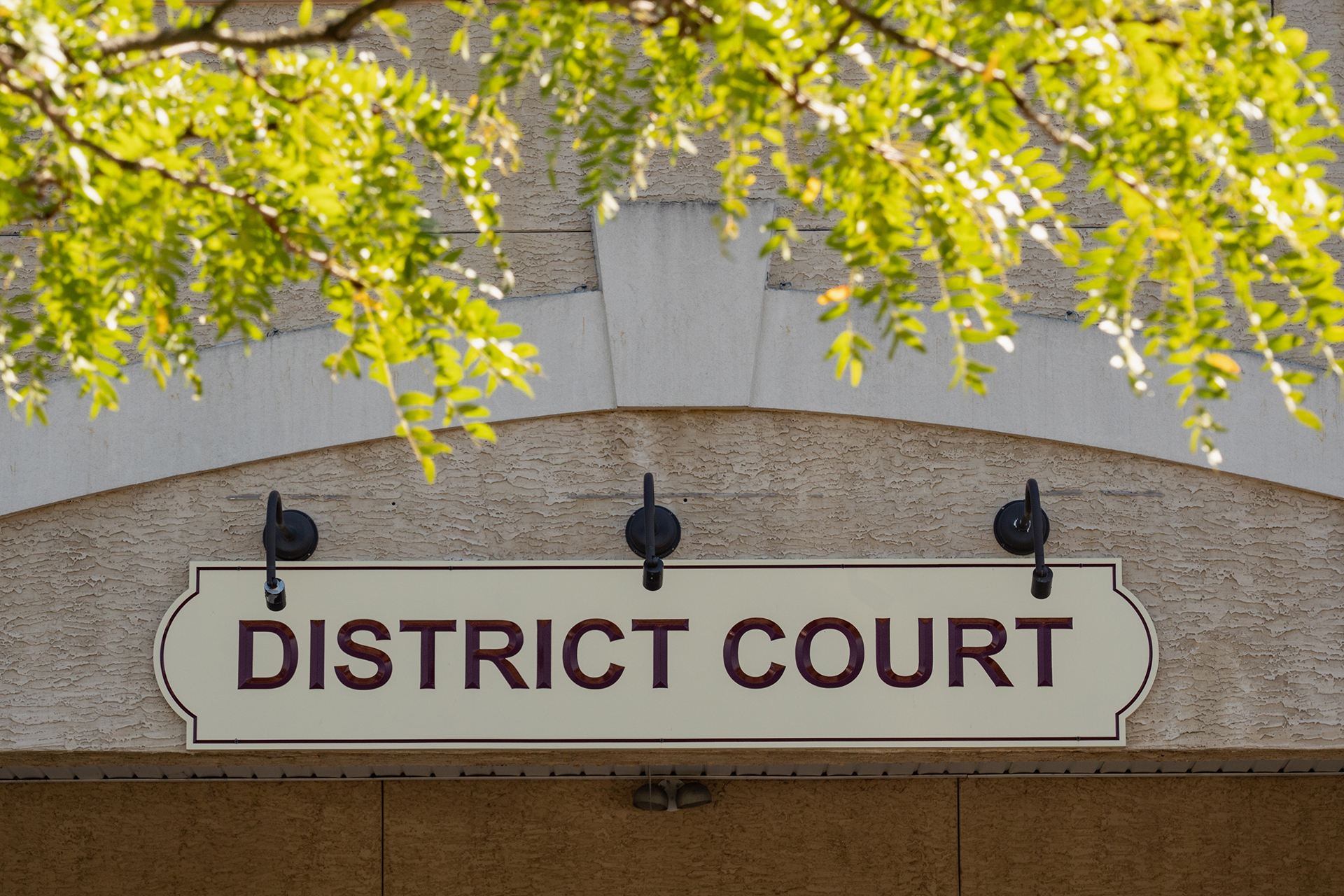 A sign displaying District Court in front of a granite building.
