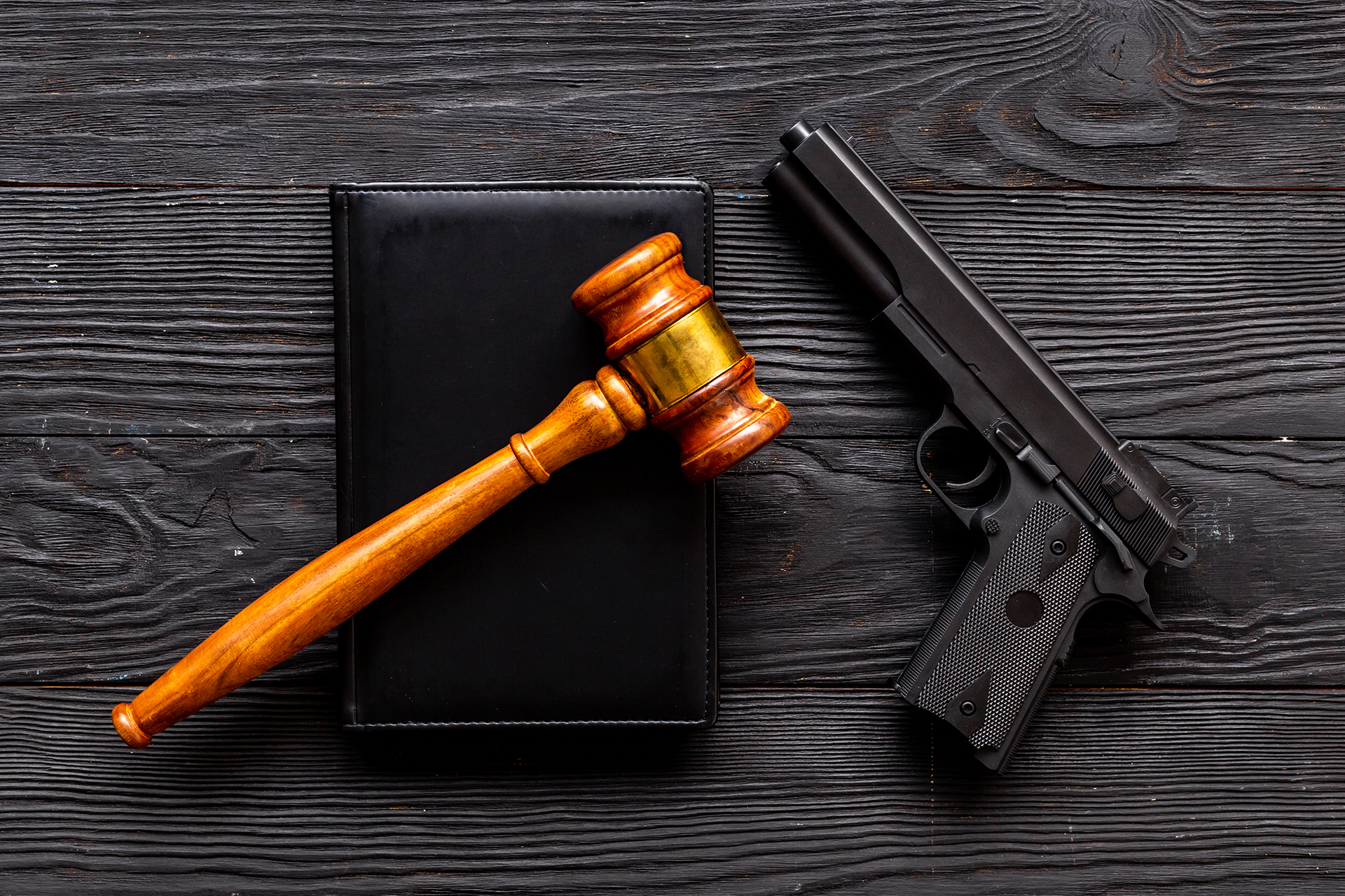 A gavel resting on a book next to a semi-automatic handgun.
