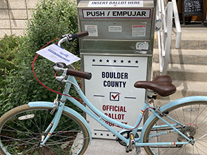 Bicycle with ballot perched on handlebars parked in front of Boulder County Drop Box