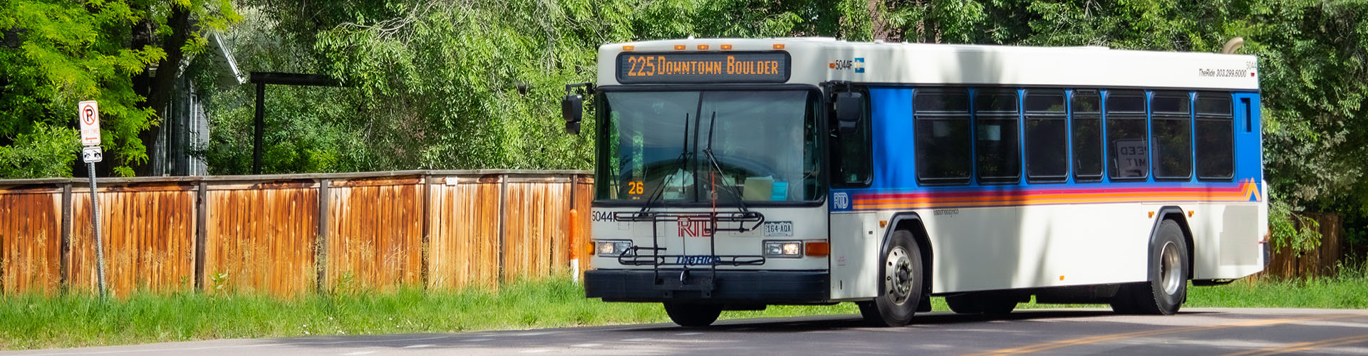 An RTD public transit bus labeled "DASH 225" travels along a road bordered by a wooden fence and greenery.