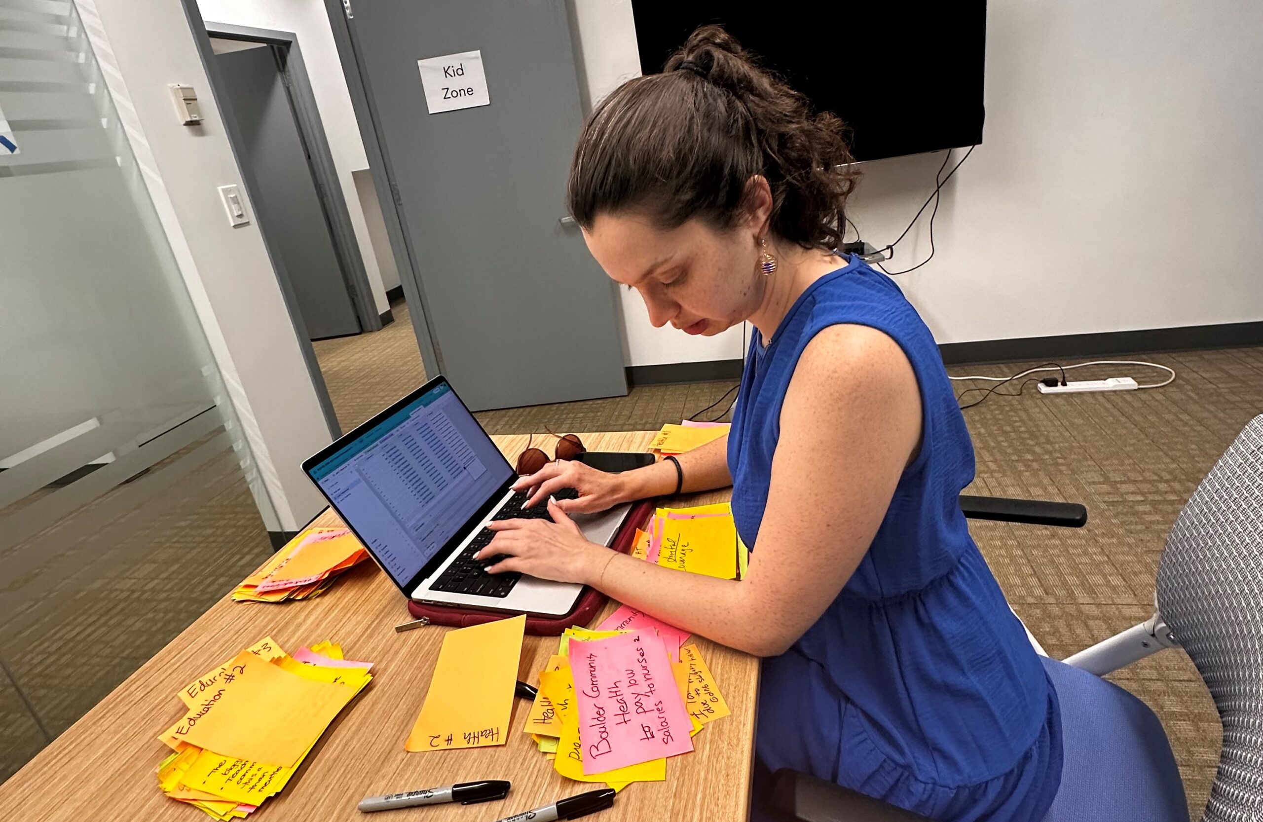 Image of a woman reading information written on post-it notes and typing the information on a laptop