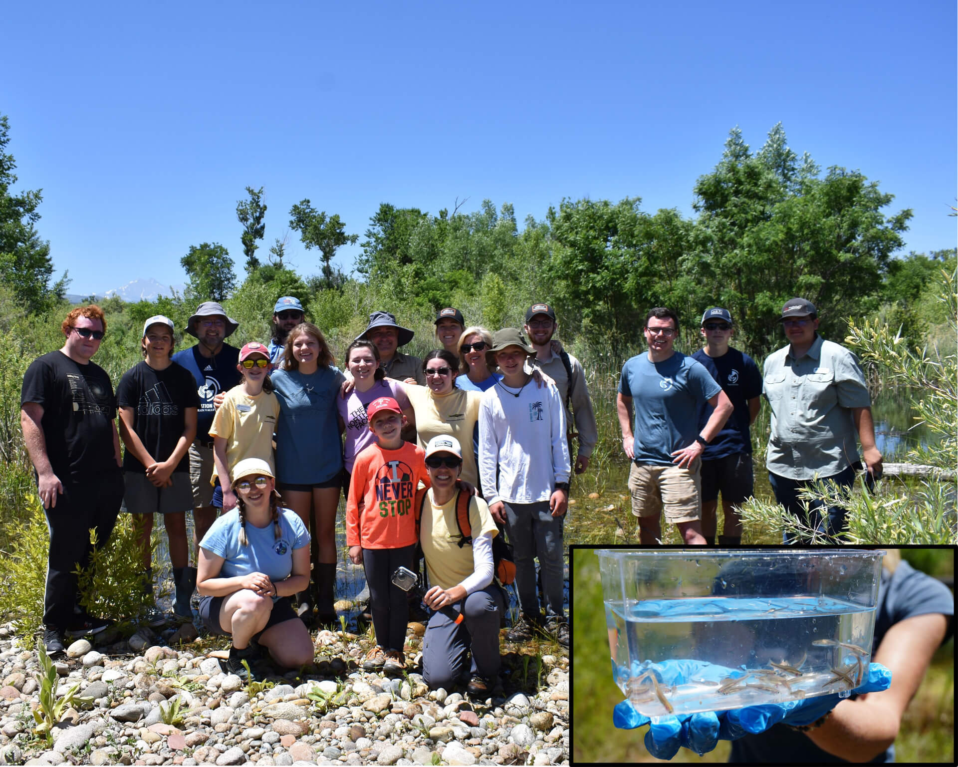 A large group of teenagers pose for a group photo near a pond and small fish bowl with tiny fish