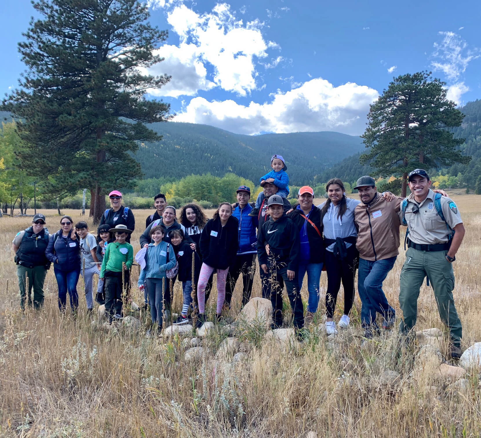 A large group of people pose for a photo in a mountain setting with park rangers