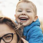 Smiling toddler riding piggyback on mom's back