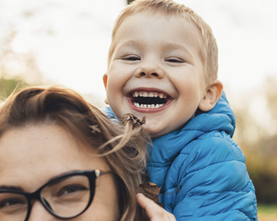 Smiling toddler riding piggyback on mom's back