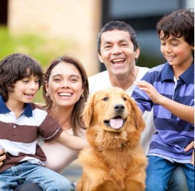 A mom, dad, two young sons and a dog kneeling down and smiling