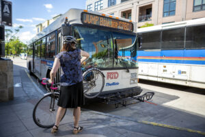 Woman placing her bicycle on the front of the bus .