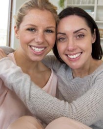 Two twenty-something year old women smiling at the camera with their arms around each other