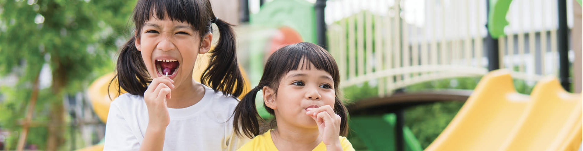 Two children smiling and enjoying lollipops outdoors