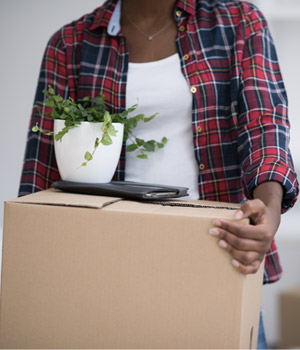 A woman carrying a box containing a potted plant during a move