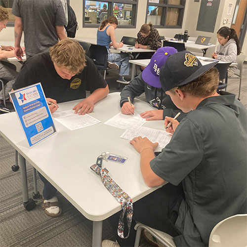 High school students sit at a table and complete voter registration forms.