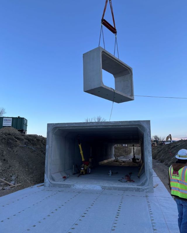 Concrete section being hoisted by a crane at a construction site with a worker observing.