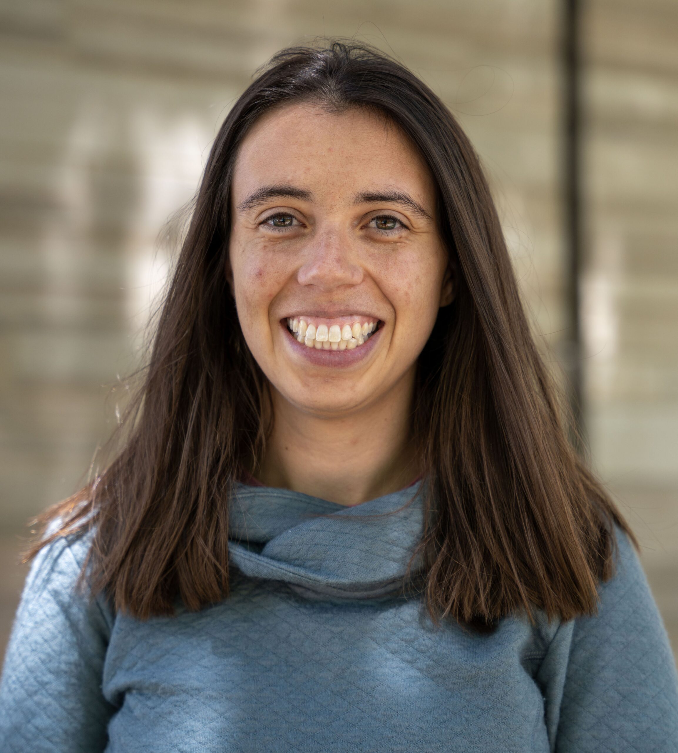Portrait of Emily, a woman with straight brown hair wearing a blue sweater.