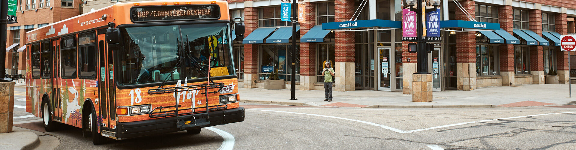 Closeup of the front of "The Hop", an orange city bus as it drives around the corner in Boulder, Colorado.
