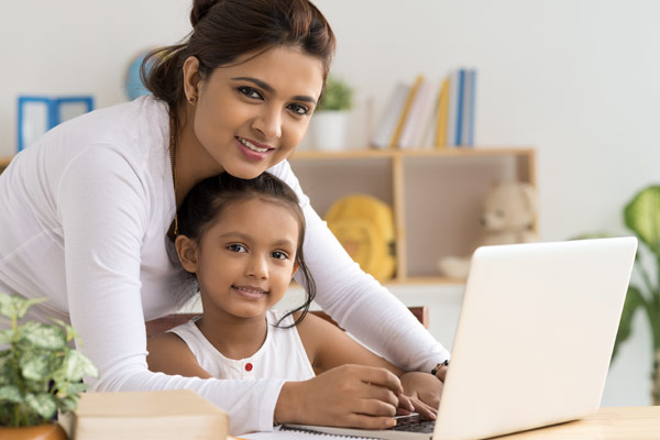 Mom and daughter smiling while working on a laptop, looking at the camera.