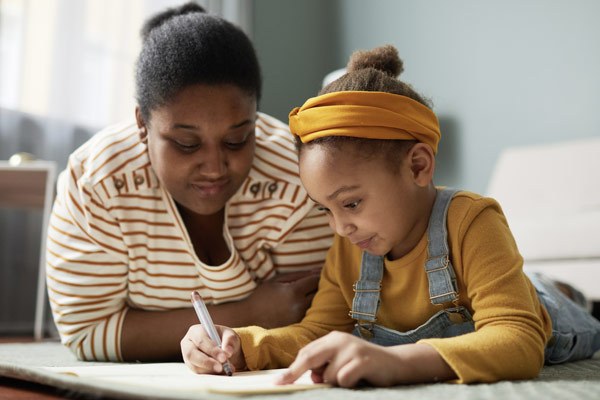Two sisters focused on writing in a notebook.