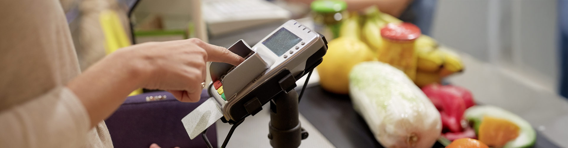 Woman entering a PIN on a payment machine at a grocery store checkout.