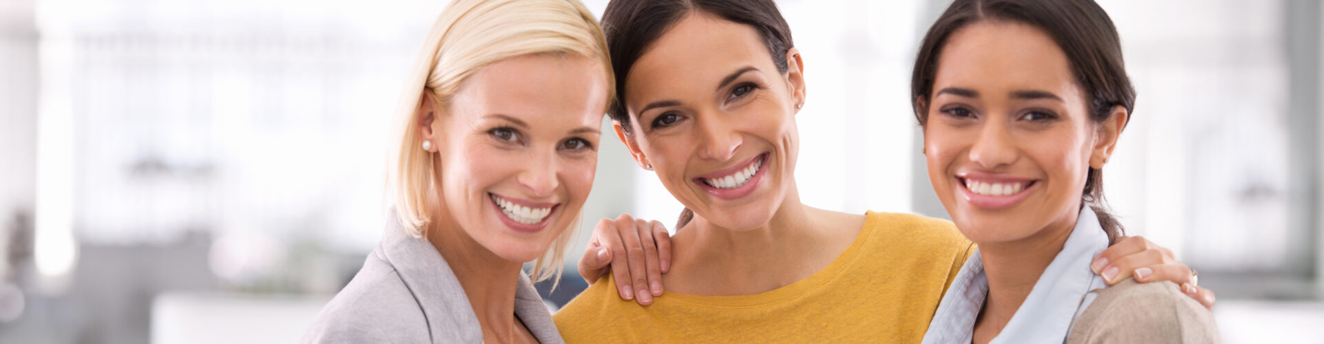 faces of three women posing together in an office setting