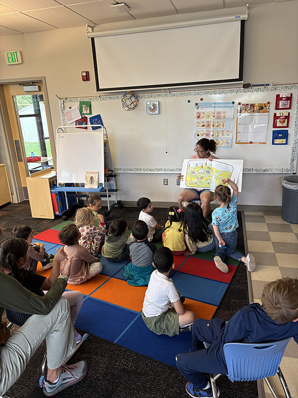 impact-education-every-child-can-learn Teacher showing and explaining a map to a group of children sitting on the carpet during a lesson.