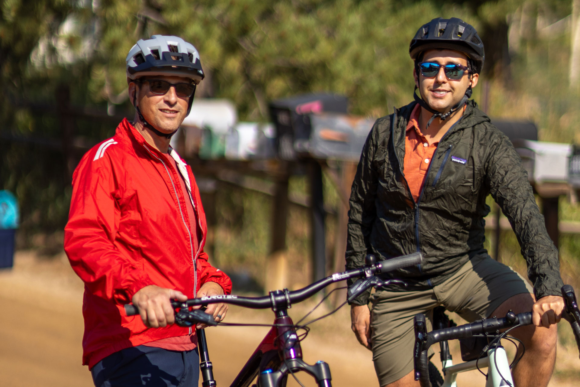 Two adults wearing safety helmets and standing with their bikes.