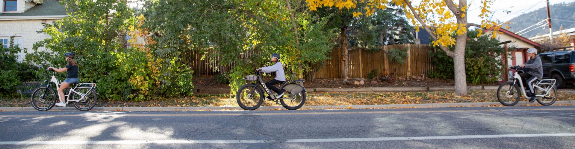 Three children riding on ebikes following in a line, on the road on a sunny fall day.