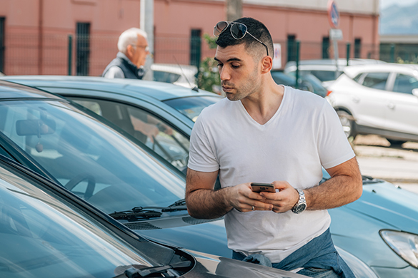 A man holding a cell phone is looking into a car through the front windshield.