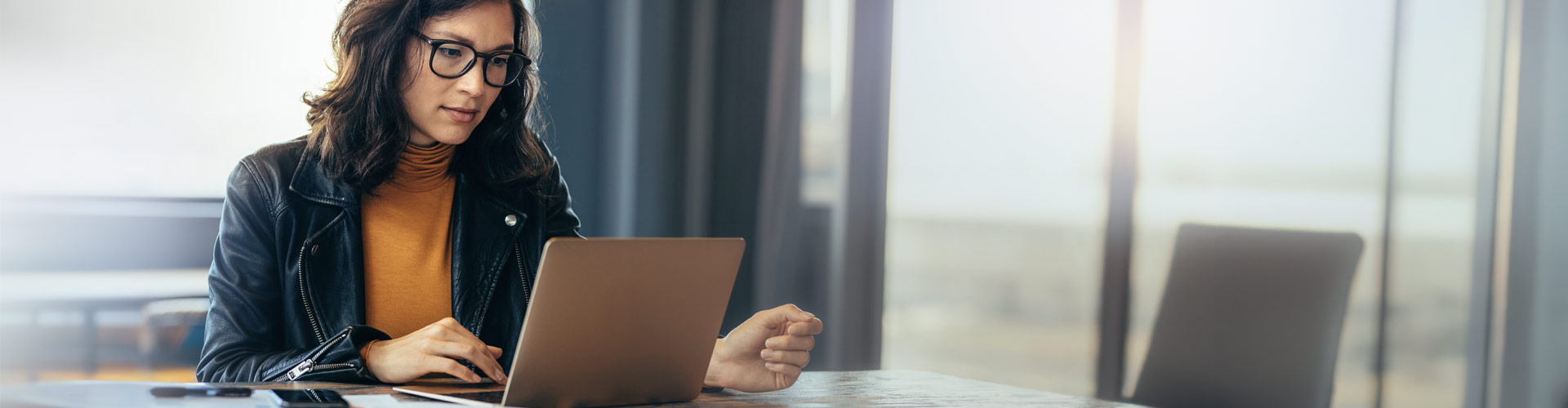 Focused professional woman wearing glasses and working on a laptop at a desk