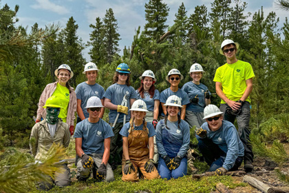 A Youth Corps team poses for a group photo in a forested area.