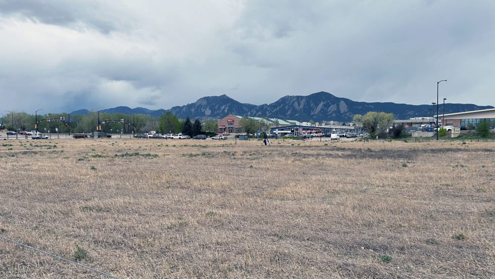 A dusty, barren field below with Boulder Flatirons and a cloudy sky.