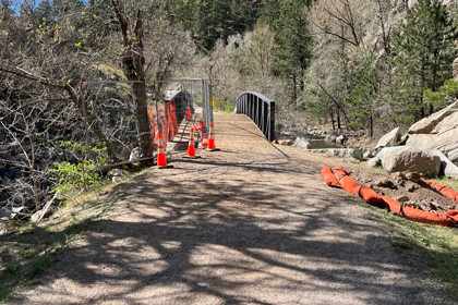 A trail leads to a bridge with a fence that blocks a hole in the ground.