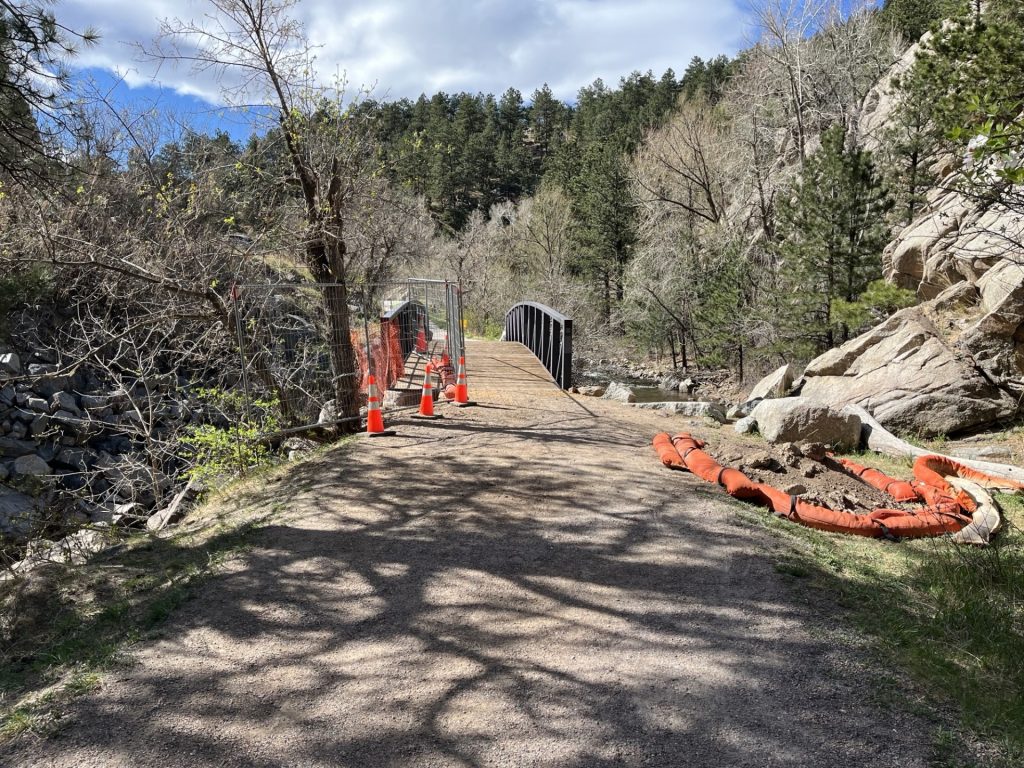 A trail leads to a bridge with a fence that blocks a hole in the ground