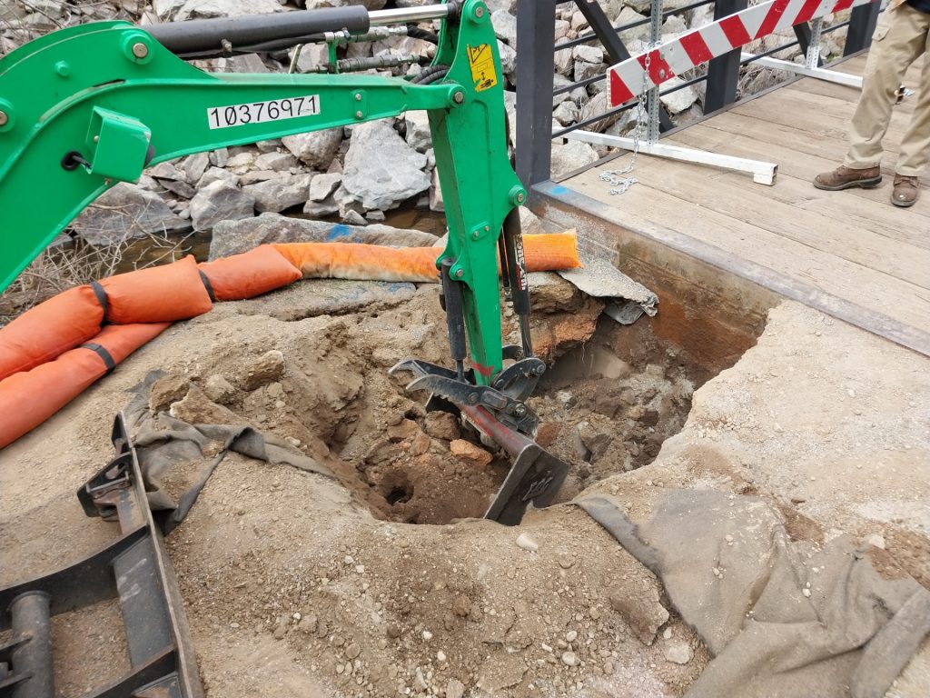 Machinery removes dirt in front of the bridge to expose the hole below the trail surface.