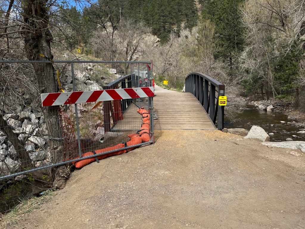A fence blocks reduces the trail width in front of a bridge.