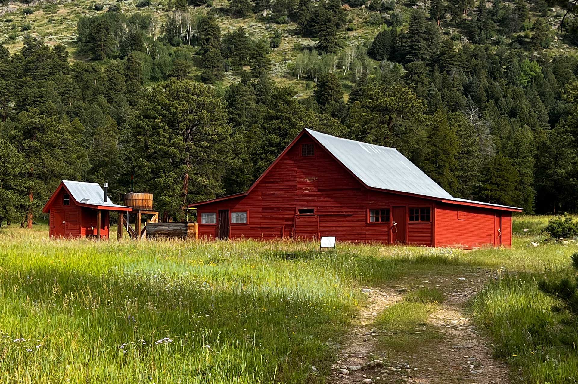 The historic Delonde Barn is a large red barn that sits in a green meadow surrounded by mountains.