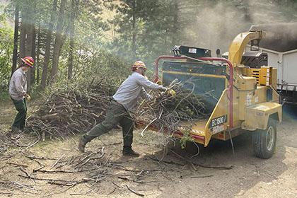 Members of the Four Mile Fire Crew use a chipper on slash piles during a community chipping event.