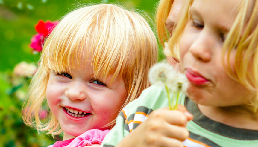 kids blowing on dandelions