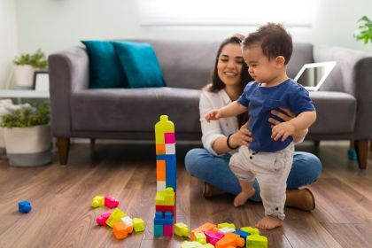 Woman and infant play with blocks in a living room.